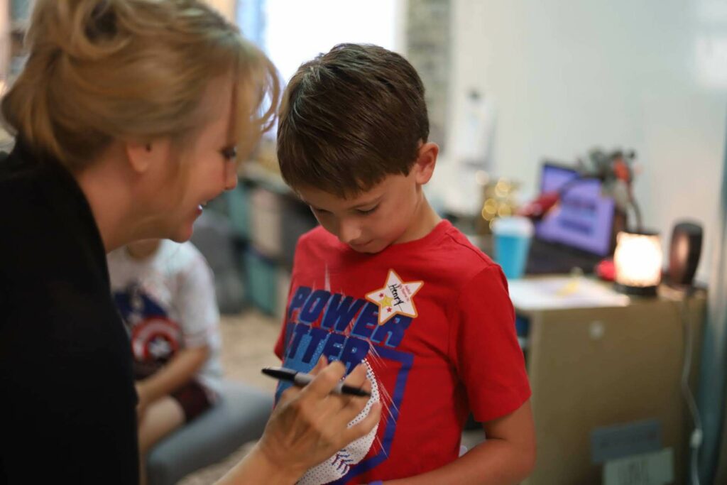 A teacher puts a star on a young student's shirt.
